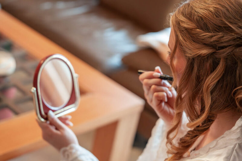 Braut schminkt sich vor deinem Spiegel beim Getting Ready vor ihrer Hochzeit
