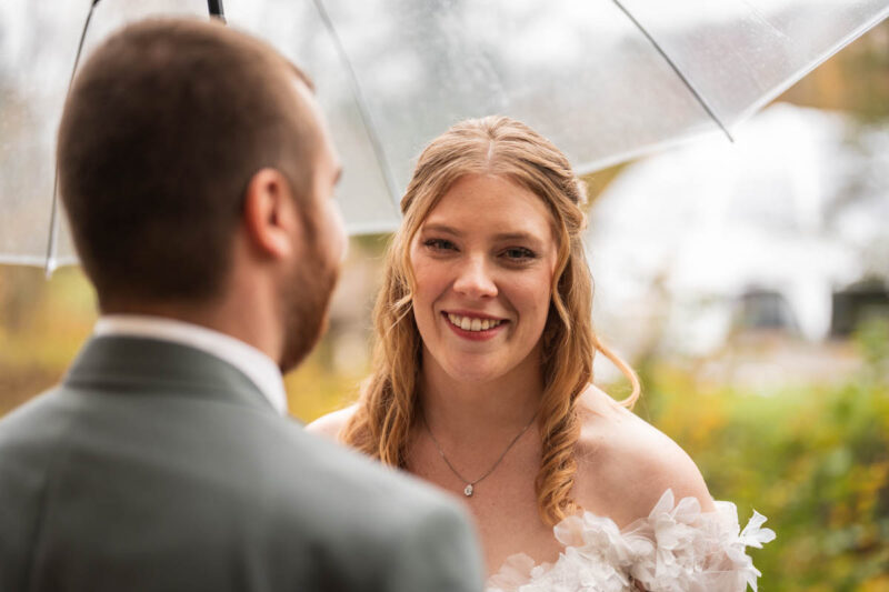 Braut steht im Fokus und blickt über die Schulter des Bräutigams in die Kamera