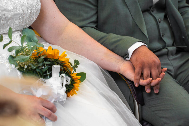 Brautpaar hält während der standesamtlichen Trauung Händchen